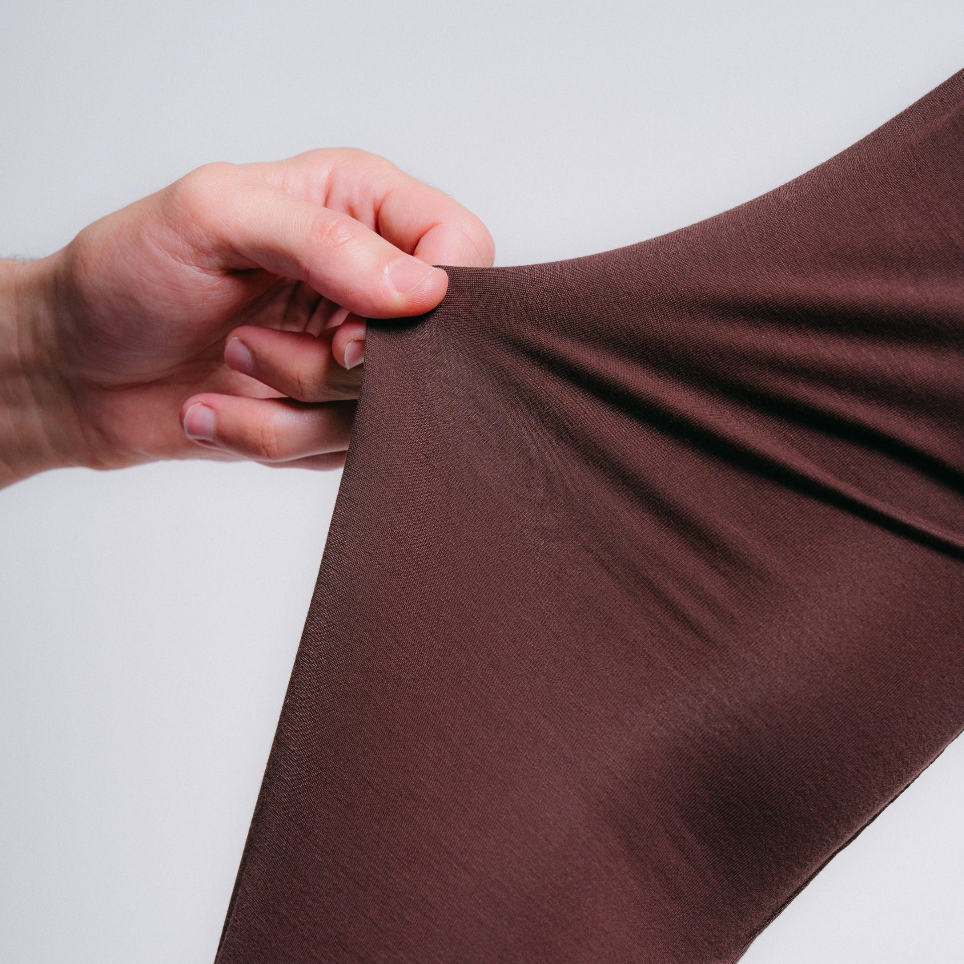 Brown fabric being stretched by a hand on a light gray background